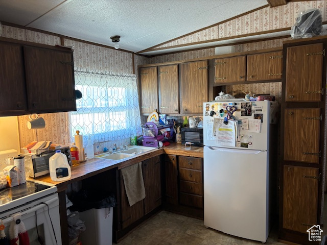 Kitchen with freestanding refrigerator, wallpapered walls, electric stove, a sink, and lofted ceiling
