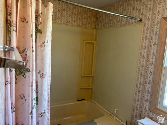 Full bath featuring wallpapered walls and shower / tub combo