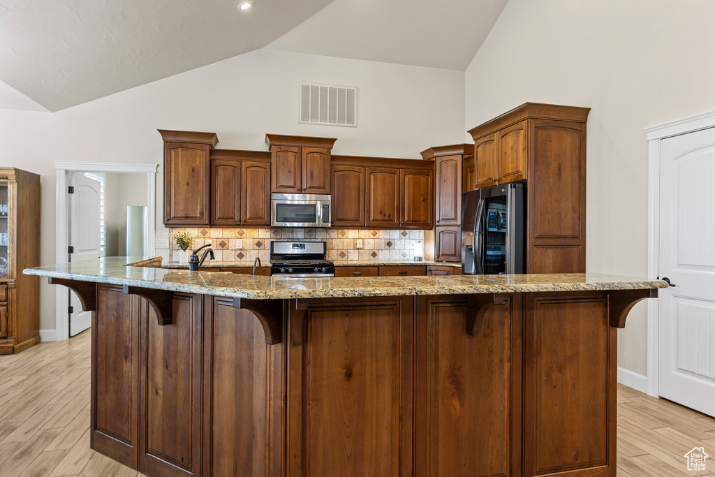 Kitchen with appliances with stainless steel finishes, a breakfast bar area, high vaulted ceiling, decorative backsplash, and light stone counters
