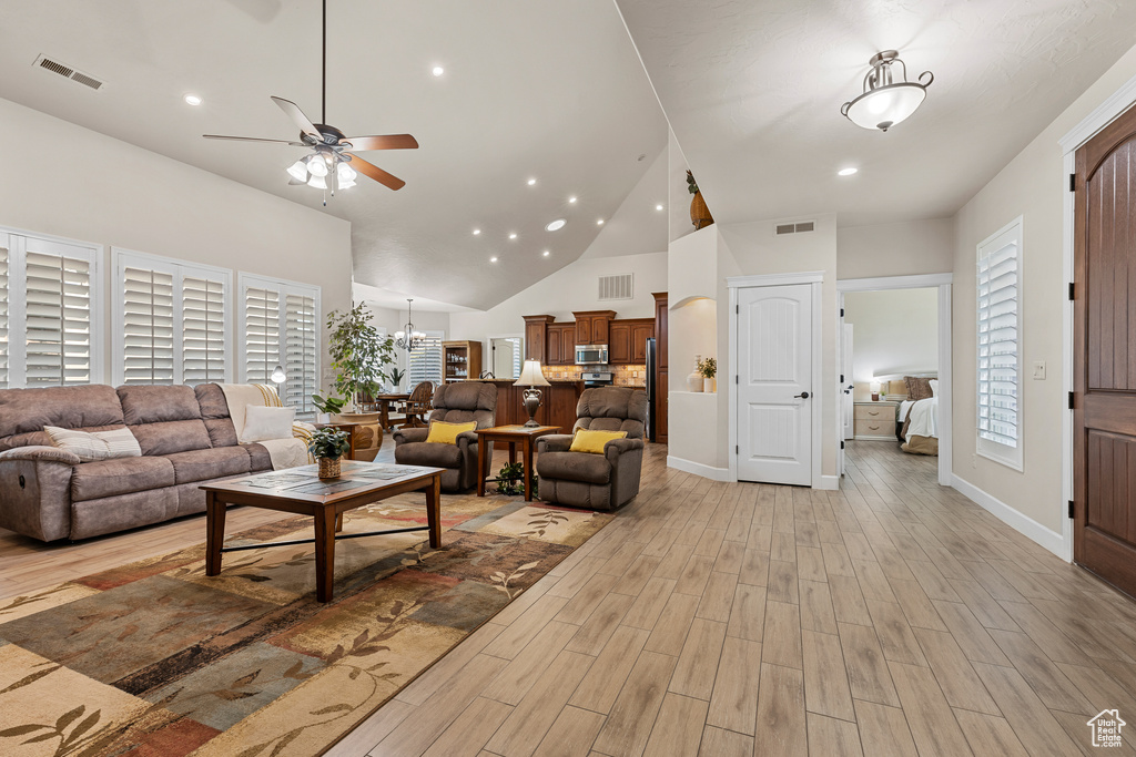 Living area with a ceiling fan, light wood-type flooring, high vaulted ceiling, a chandelier, and baseboards