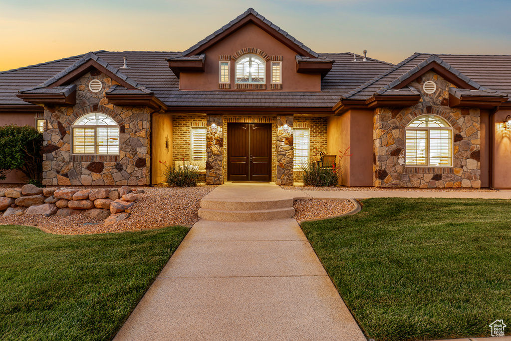 View of front of home with stone siding, a tile roof, a front lawn, and stucco siding