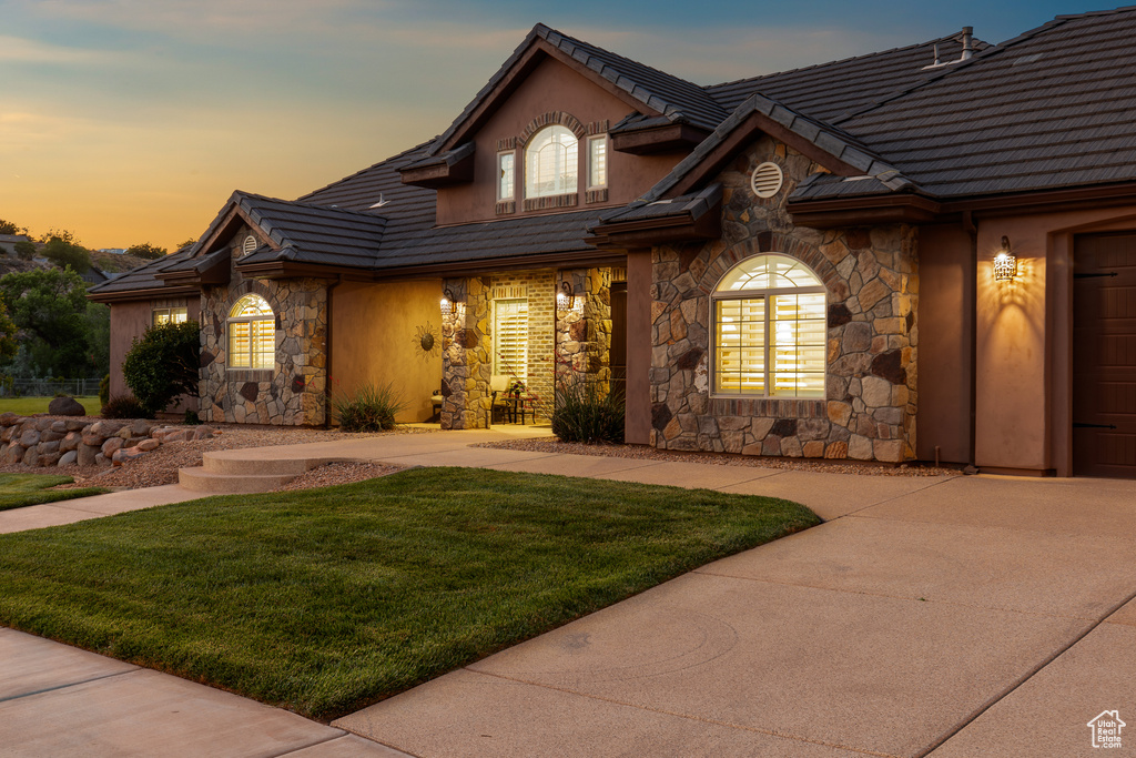 View of front of house featuring stone siding, a lawn, a tile roof, and concrete driveway