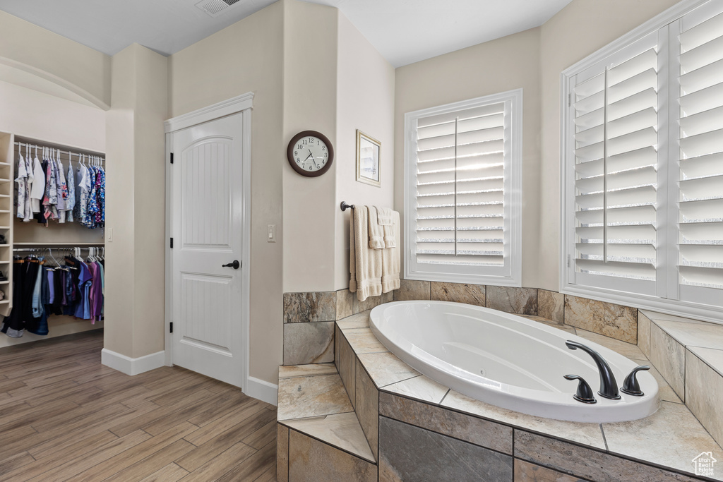 Full bathroom with a jetted tub, wood finished floors, baseboards, and a spacious closet