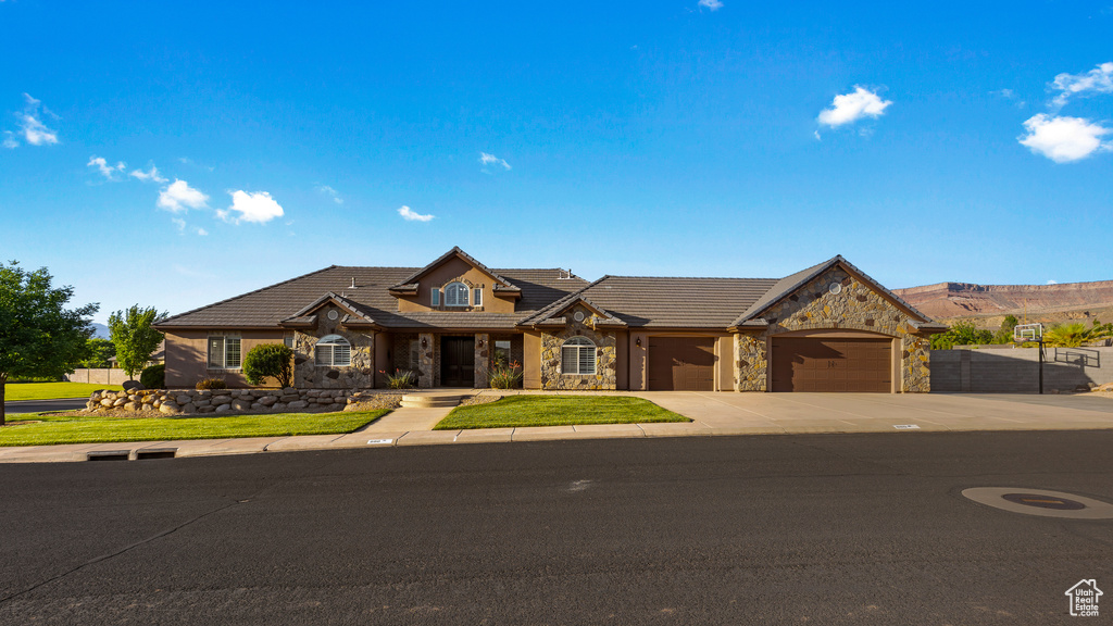 Traditional-style house with stone siding, an attached garage, driveway, and a tile roof