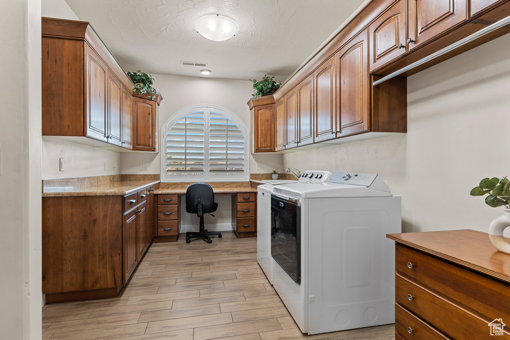 Laundry room with washer and dryer, cabinet space, a desk, light wood-style flooring, and a textured ceiling