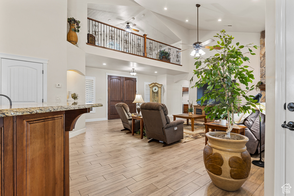 Living room featuring ceiling fan, a high ceiling, light wood finished floors, baseboards, and recessed lighting