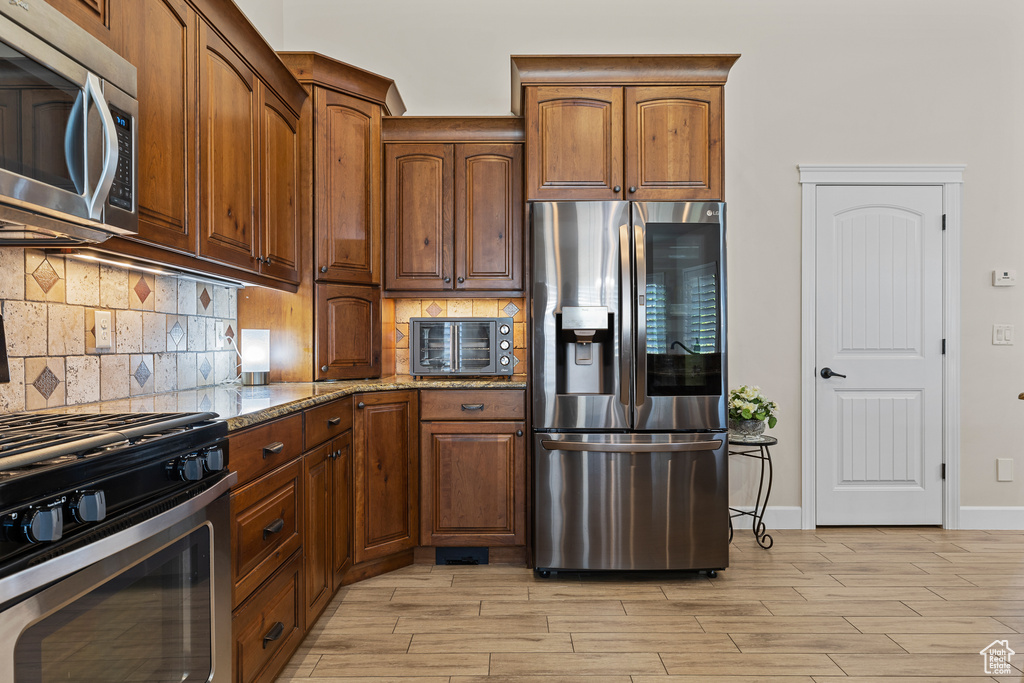 Kitchen featuring appliances with stainless steel finishes, light stone countertops, light wood-style floors, and backsplash