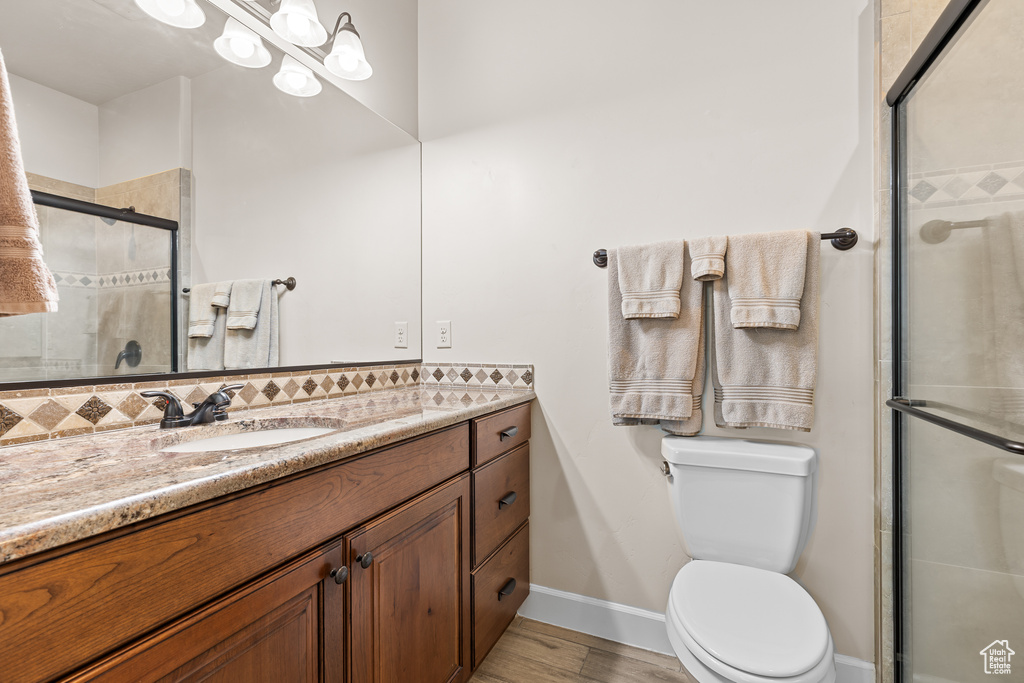 Full bathroom featuring vanity, tiled shower, wood finished floors, toilet, and baseboards