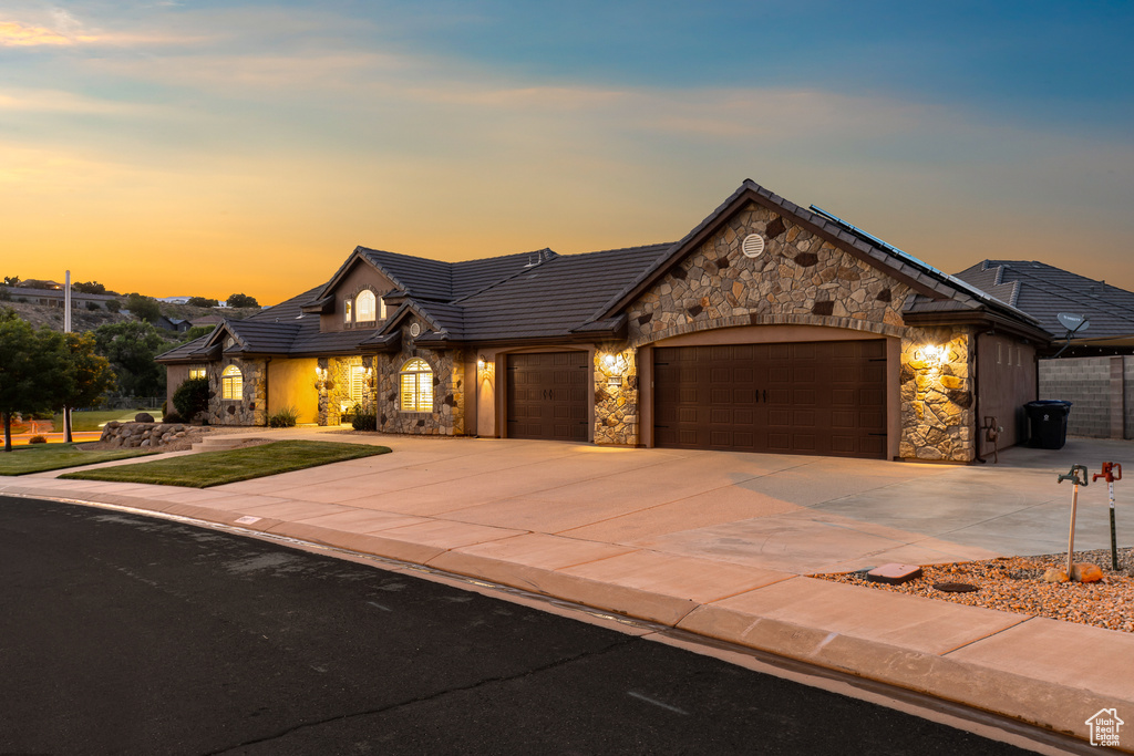 View of front of home featuring stone siding, an attached garage, driveway, a tiled roof, and a front yard