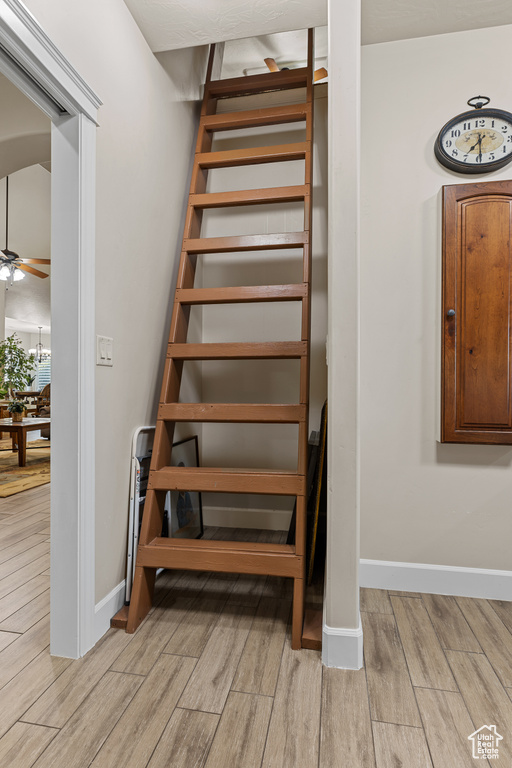 Staircase with wood finished floors, a ceiling fan, and baseboards