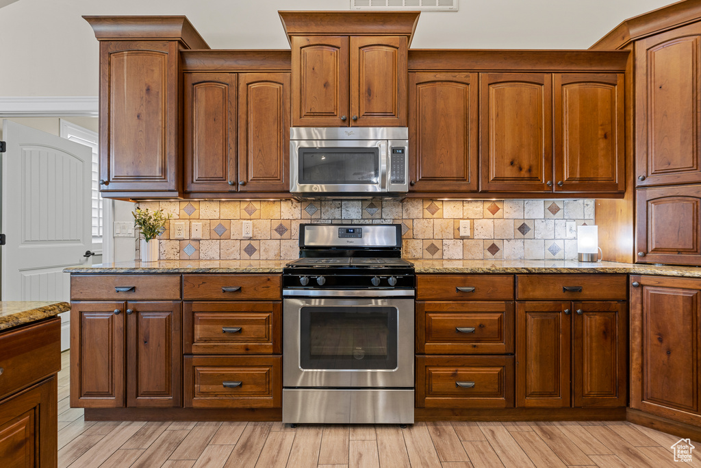 Kitchen with stainless steel appliances, light stone counters, tasteful backsplash, and light wood-type flooring