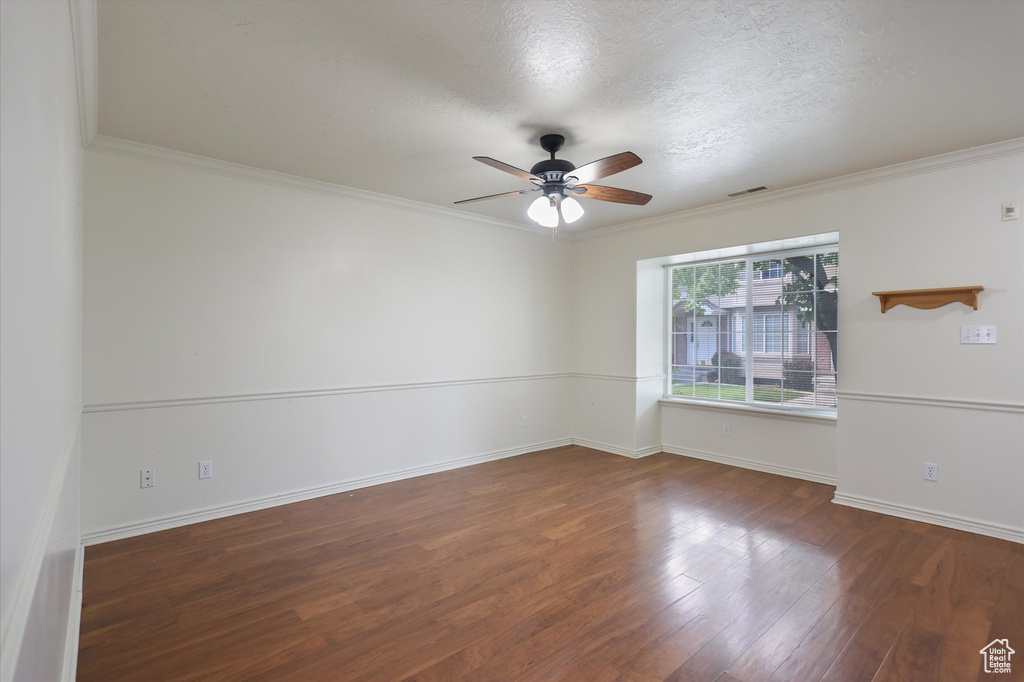 Empty room featuring a ceiling fan, wood finished floors, baseboards, ornamental molding, and a textured ceiling