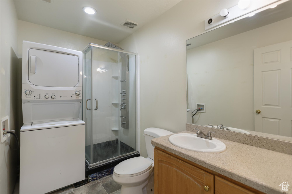 Full bath featuring estacked washer and dryer, toilet, a stall shower, and vanity