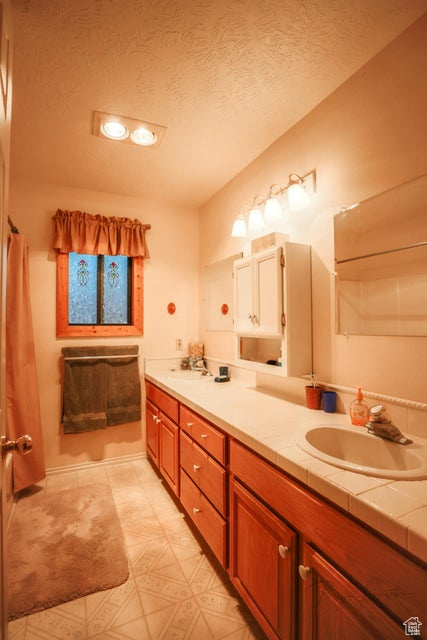 Full bath with double vanity, a textured ceiling, and tile patterned floors