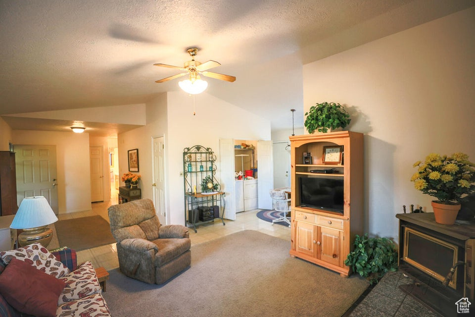 Living area featuring vaulted ceiling, a ceiling fan, independent washer and dryer, a textured ceiling, and carpet floors