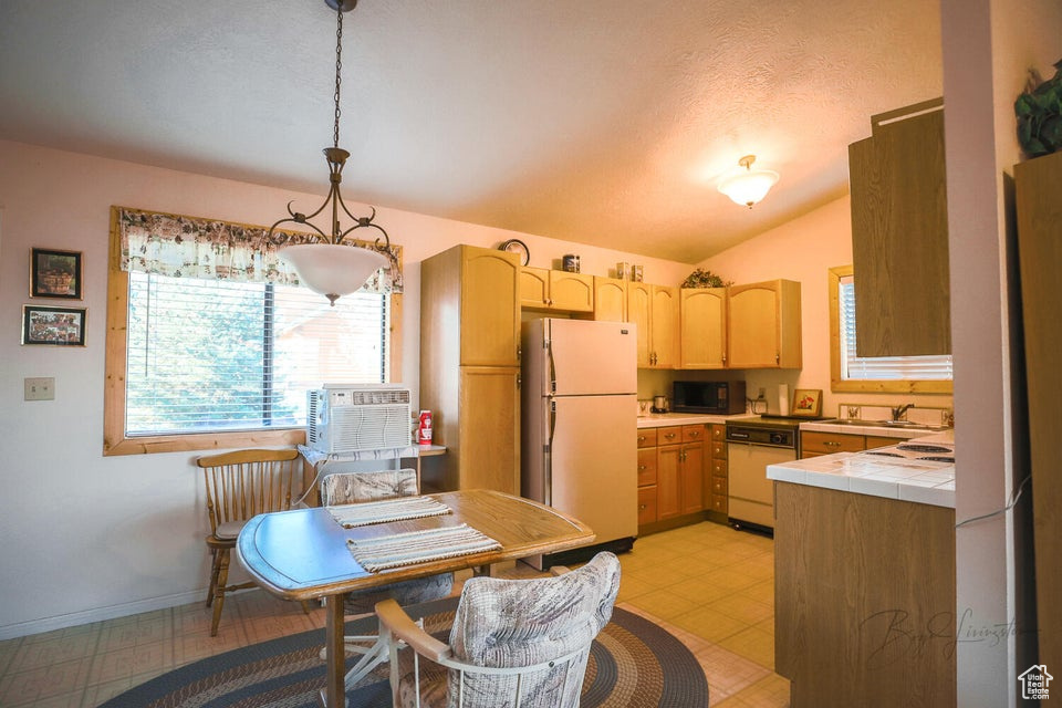 Kitchen featuring white appliances, tile counters, light flooring, vaulted ceiling, and light brown cabinetry