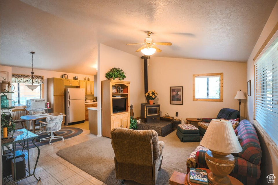 Living area with vaulted ceiling, a wood stove, plenty of natural light, ceiling fan, and a textured ceiling