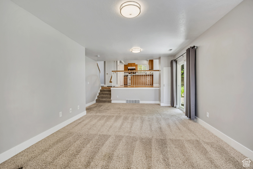 Unfurnished living room with light carpet, baseboards, and stairway