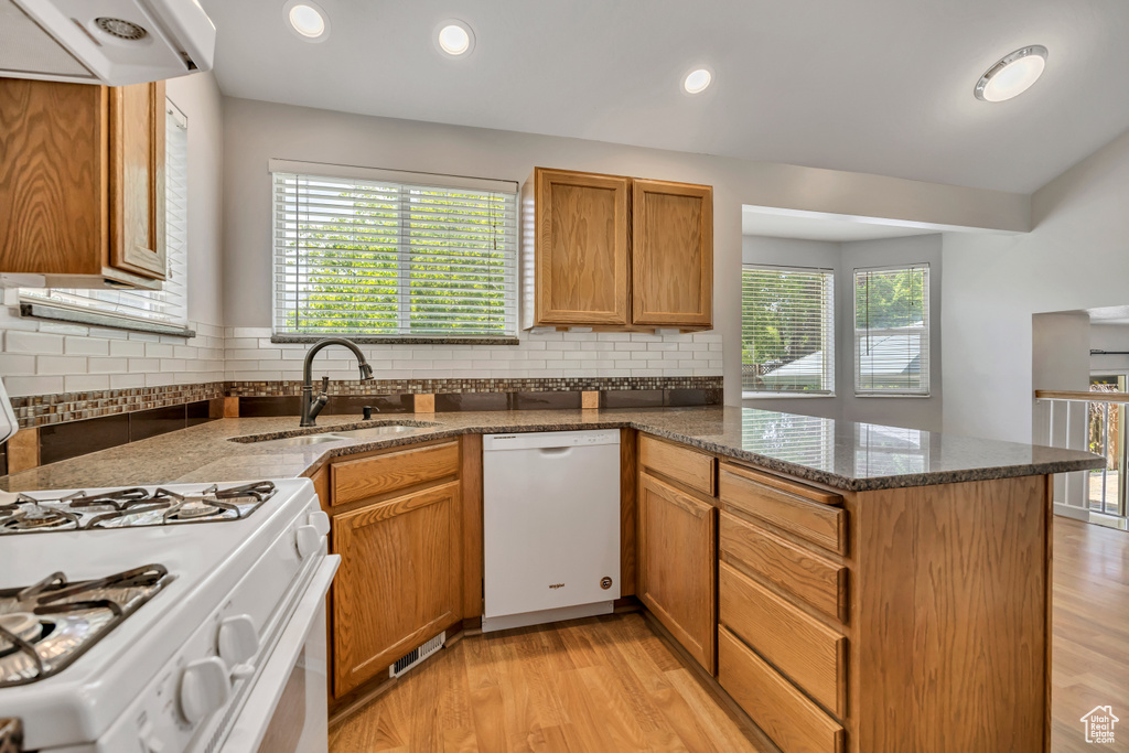 Kitchen featuring white appliances, a sink, a peninsula, light wood-type flooring, and recessed lighting