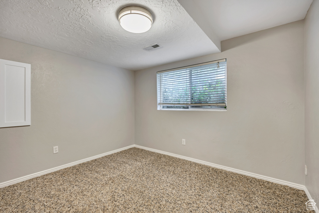 Carpeted empty room featuring a textured ceiling and baseboards