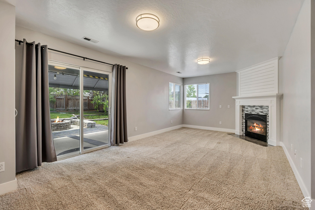 Unfurnished living room featuring carpet, a tile fireplace, baseboards, and a textured ceiling