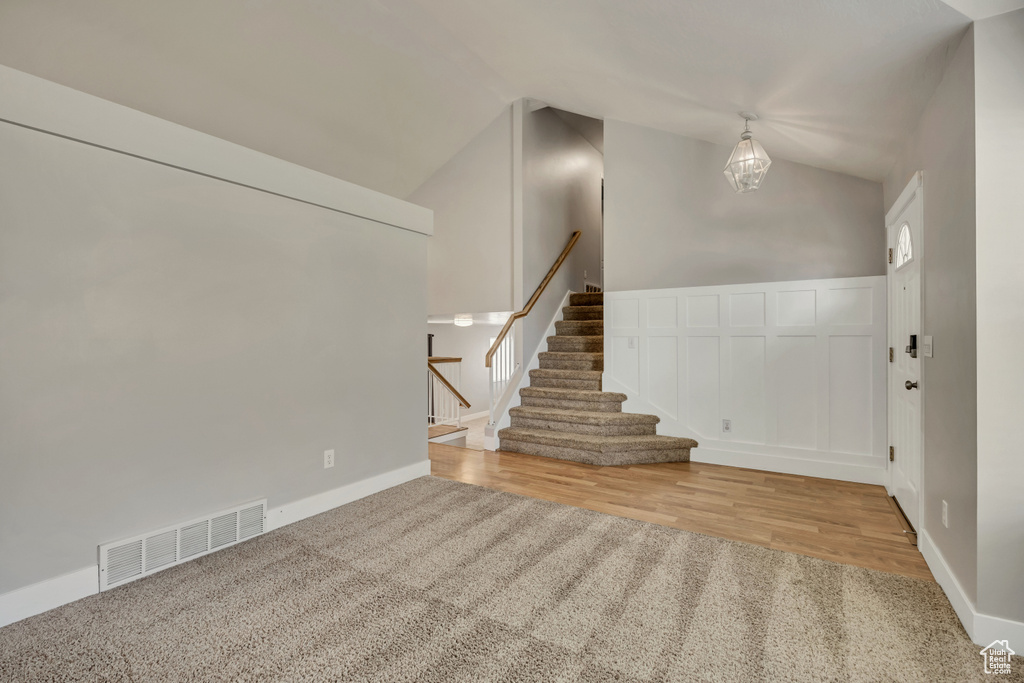 Entryway featuring lofted ceiling, stairway, a chandelier, wood finished floors, and carpet
