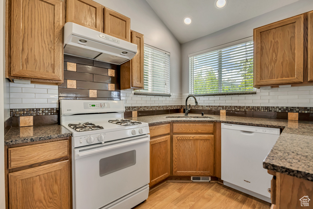 Kitchen featuring white appliances, a sink, lofted ceiling, under cabinet range hood, and decorative backsplash