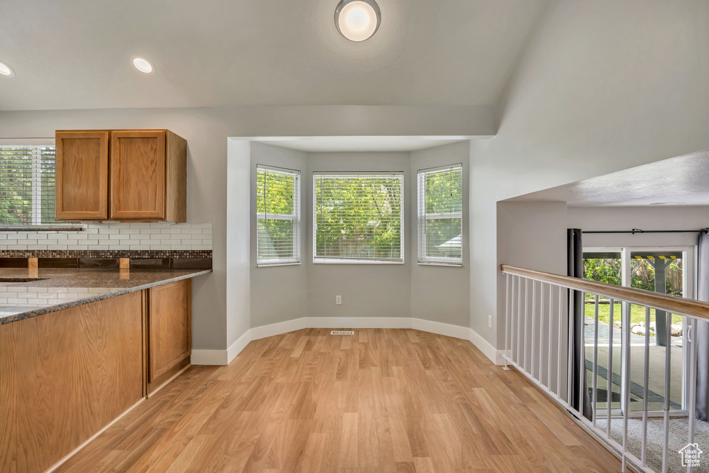 Kitchen featuring light wood finished floors, brown cabinets, backsplash, baseboards, and dark stone countertops