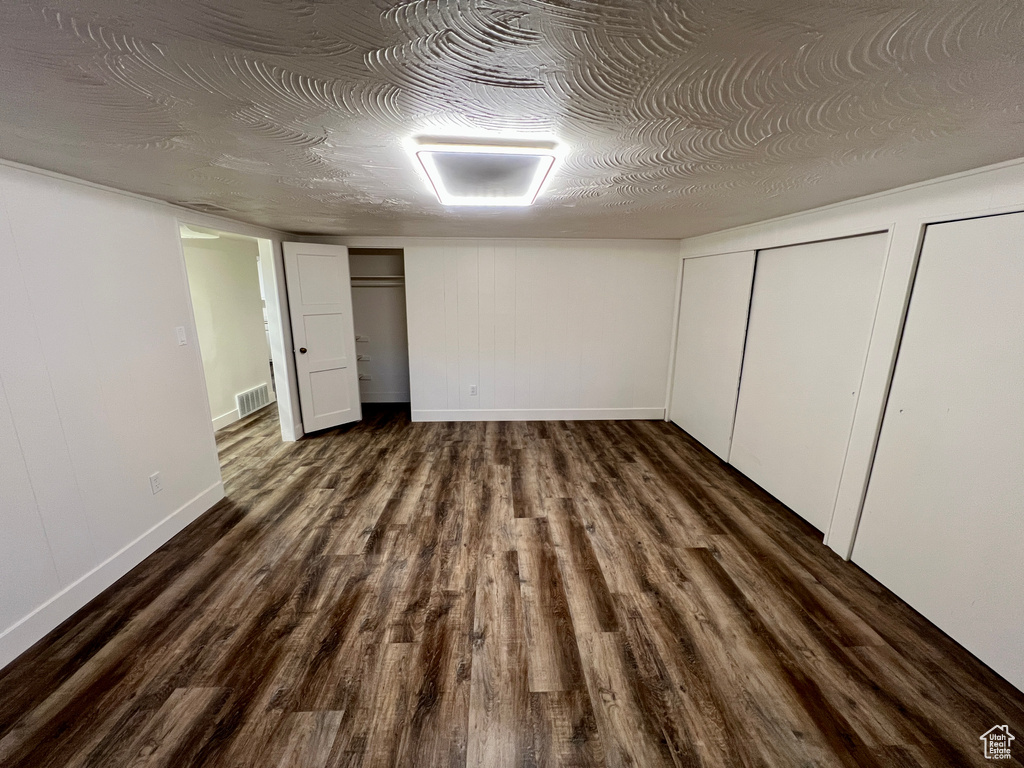 Unfurnished bedroom with two closets, dark wood-style flooring, and baseboards