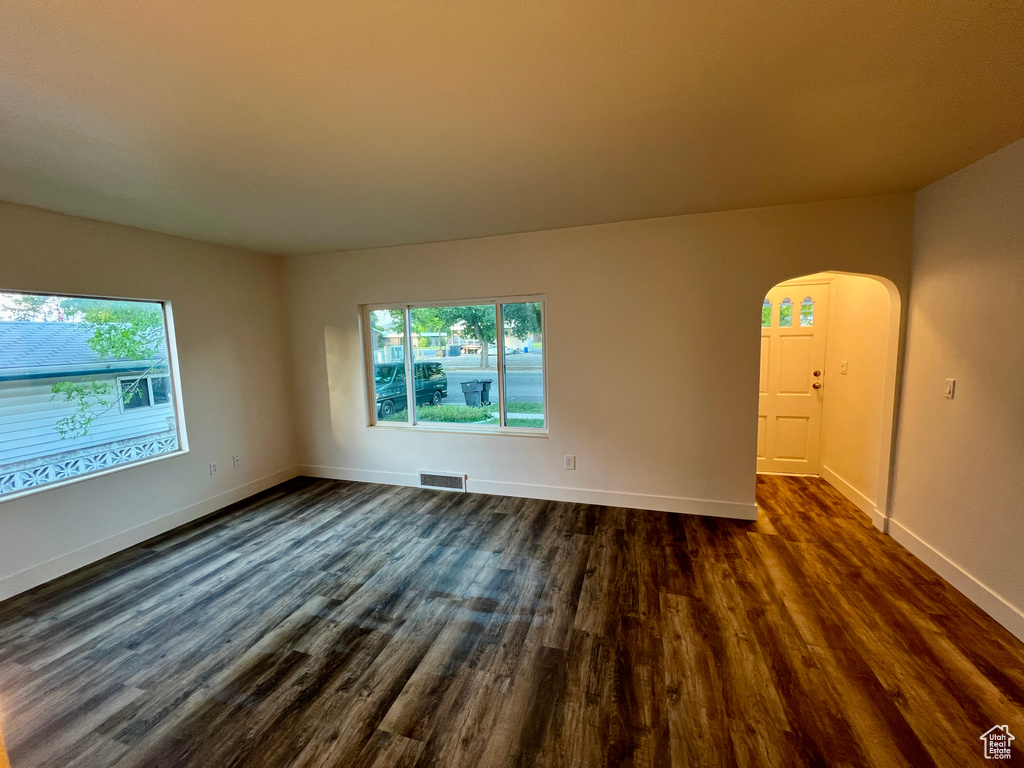 Spare room featuring arched walkways, healthy amount of natural light, dark wood-style floors, and baseboards