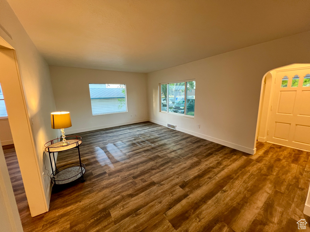 Empty room with dark wood-style flooring, baseboards, and arched walkways