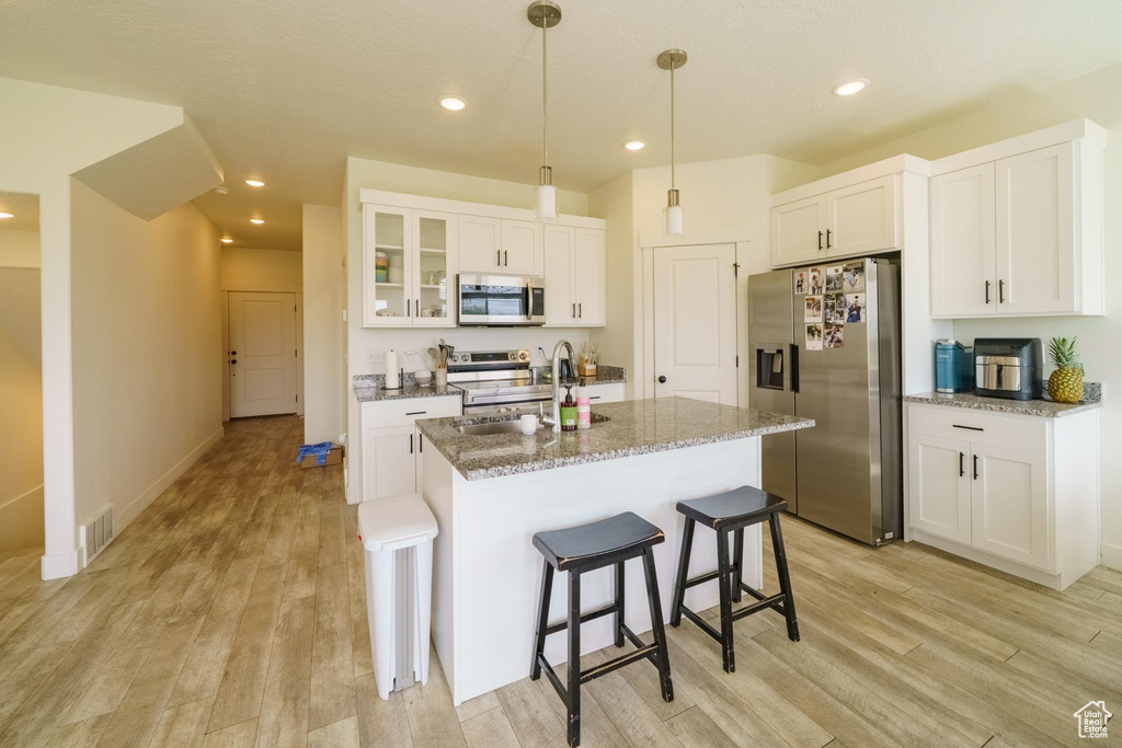 Kitchen with stainless steel appliances, light wood finished floors, a breakfast bar, white cabinetry, and recessed lighting