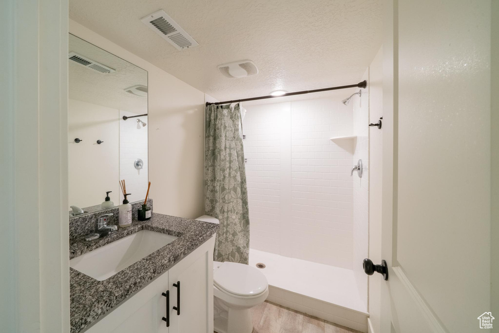 Full bath with vanity, toilet, a tile shower, a textured ceiling, and wood finished floors