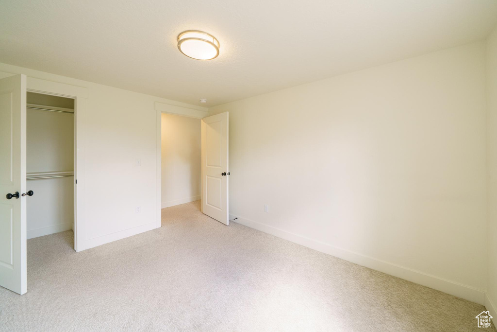 Unfurnished bedroom featuring light carpet, a closet, and baseboards