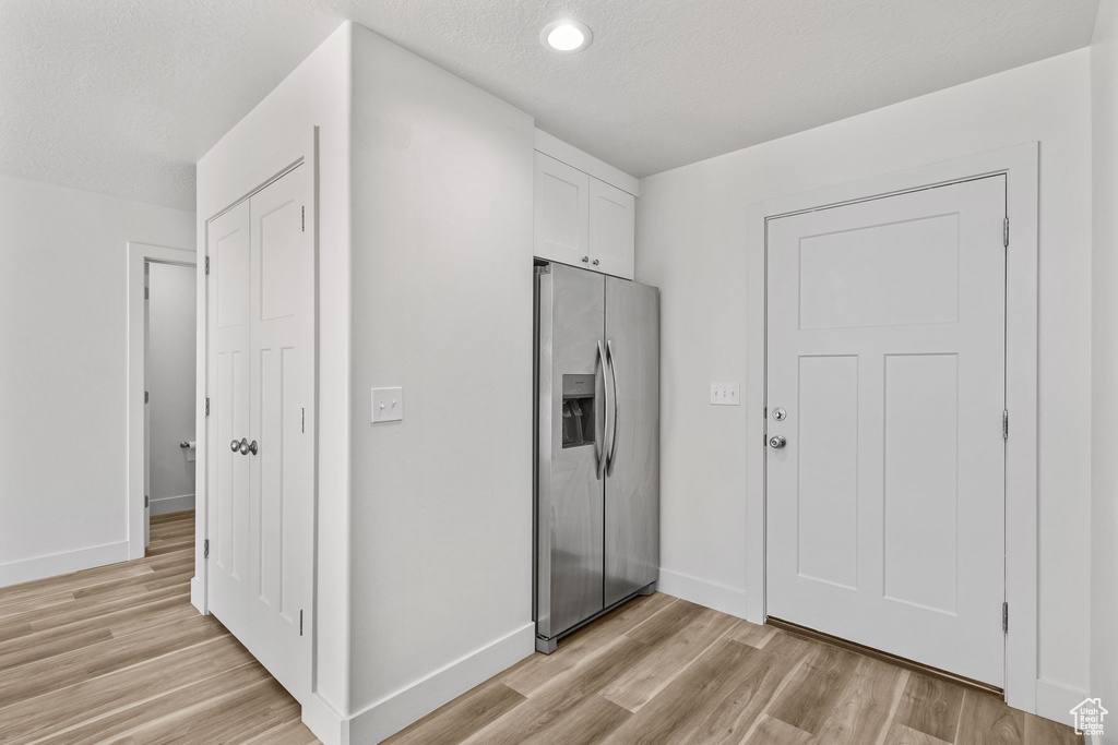 Kitchen with stainless steel refrigerator with ice dispenser, light wood finished floors, white cabinetry, baseboards, and recessed lighting