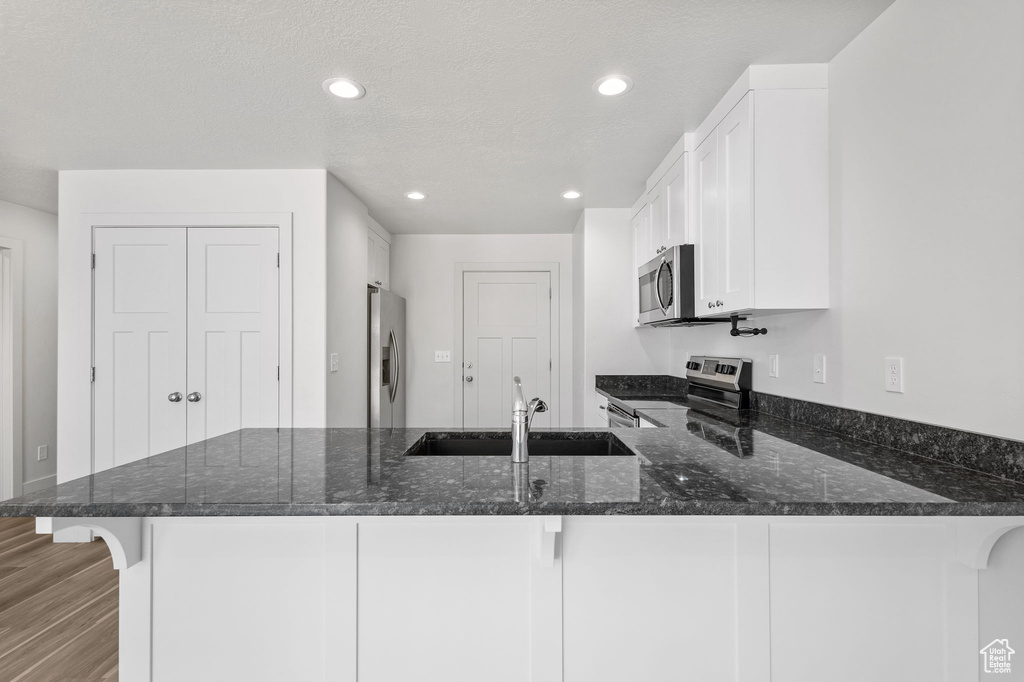 Kitchen with appliances with stainless steel finishes, a sink, a peninsula, dark stone countertops, and white cabinets