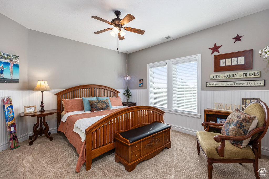 Carpeted bedroom featuring a wainscoted wall and a ceiling fan