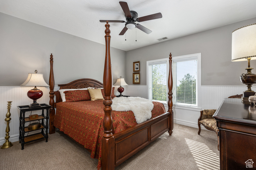 Bedroom with light colored carpet, a wainscoted wall, ceiling fan, and baseboards