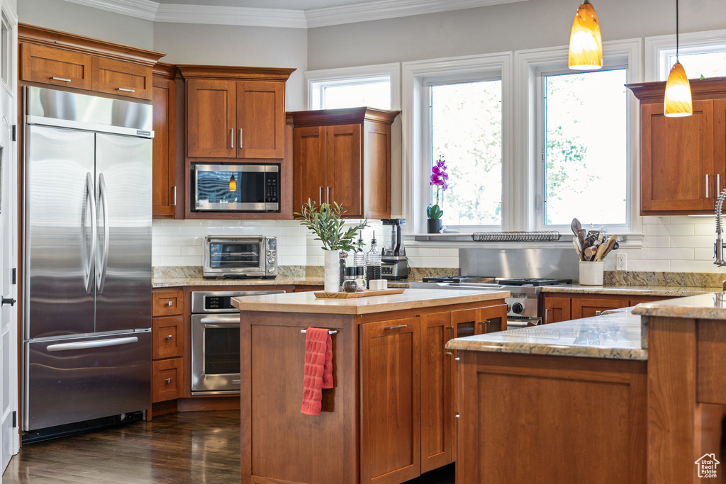 Kitchen with appliances with stainless steel finishes, plenty of natural light, ornamental molding, brown cabinetry, and backsplash