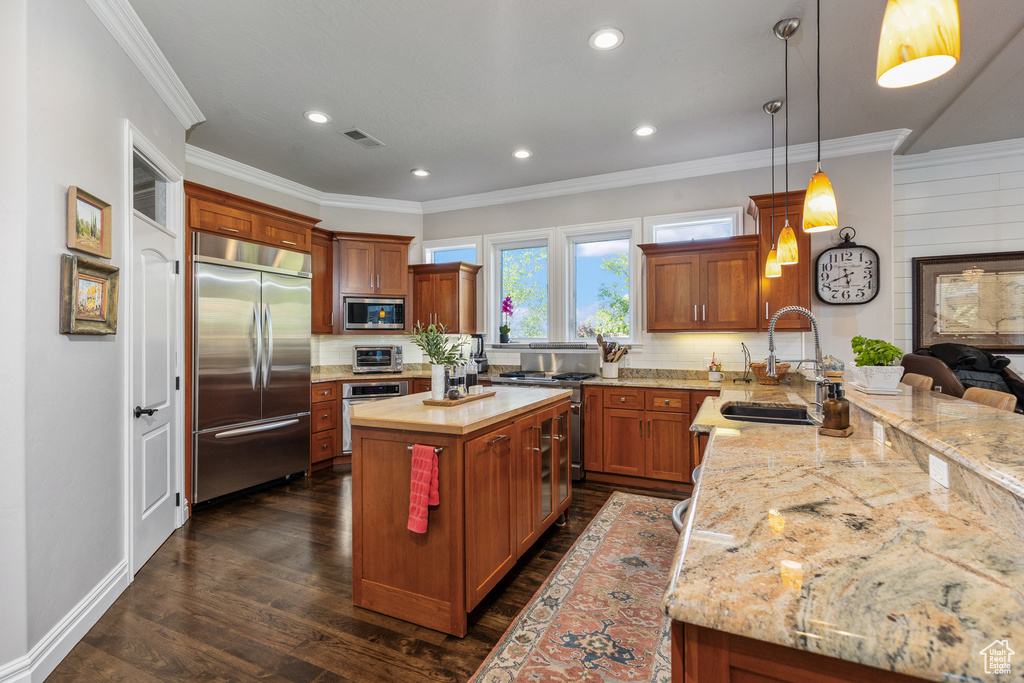 Kitchen featuring built in appliances, a sink, tasteful backsplash, crown molding, and a peninsula