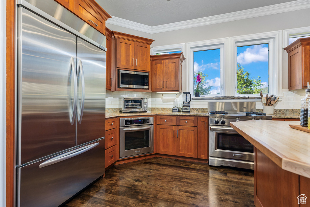 Kitchen featuring built in appliances, crown molding, tasteful backsplash, dark wood-style flooring, and brown cabinets