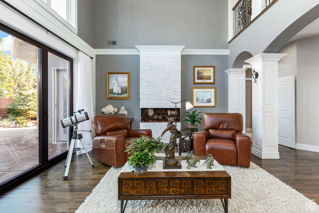Living room featuring a towering ceiling, decorative columns, arched walkways, dark wood finished floors, and baseboards