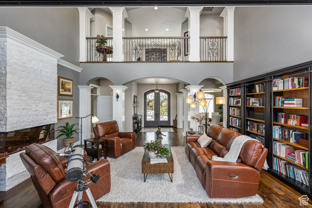Living room with ornate columns, arched walkways, wood finished floors, french doors, and a towering ceiling