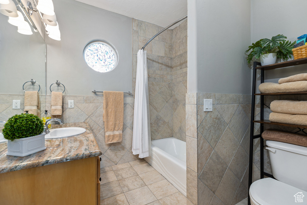 Bathroom with tile walls, tile patterned flooring, vanity, toilet, and shower / bath combo with shower curtain