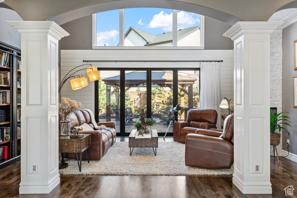 Living room with decorative columns, arched walkways, wood finished floors, plenty of natural light, and vaulted ceiling