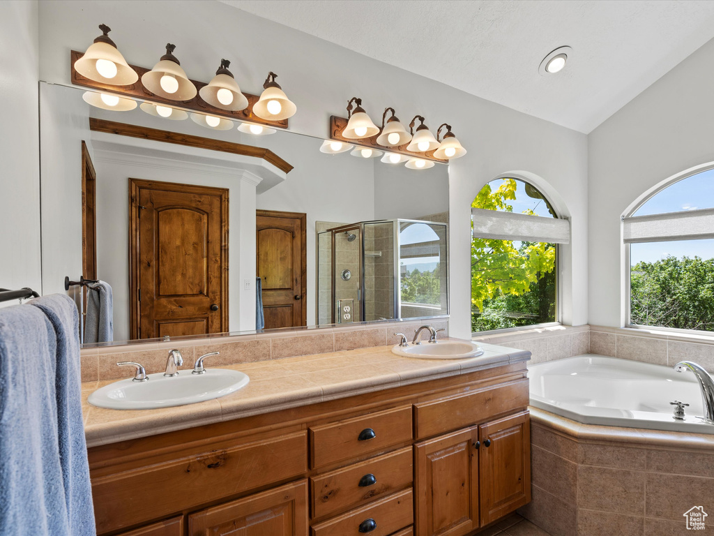 Full bath featuring double vanity, a shower stall, a bath, and vaulted ceiling