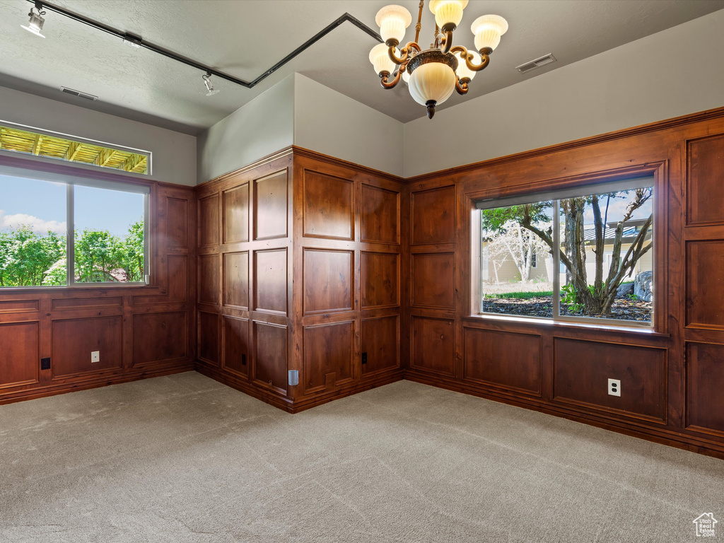 Unfurnished room with a chandelier, a decorative wall, rail lighting, light colored carpet, and healthy amount of natural light
