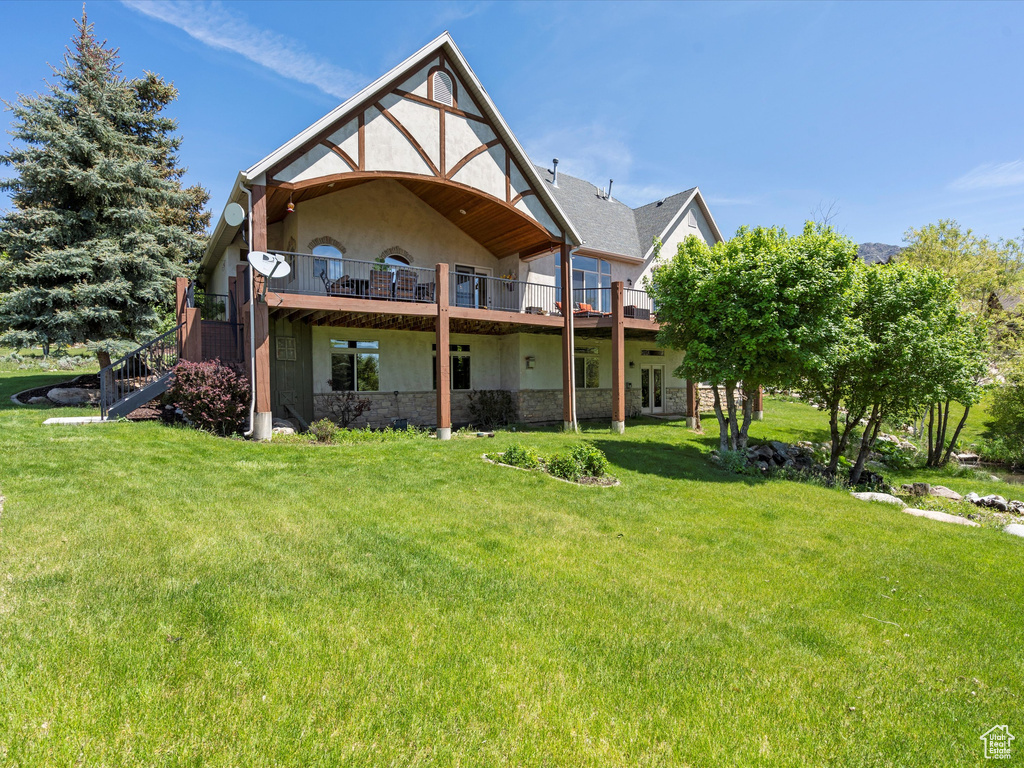 Back of property featuring a lawn, stucco siding, stone siding, a wooden deck, and stairs
