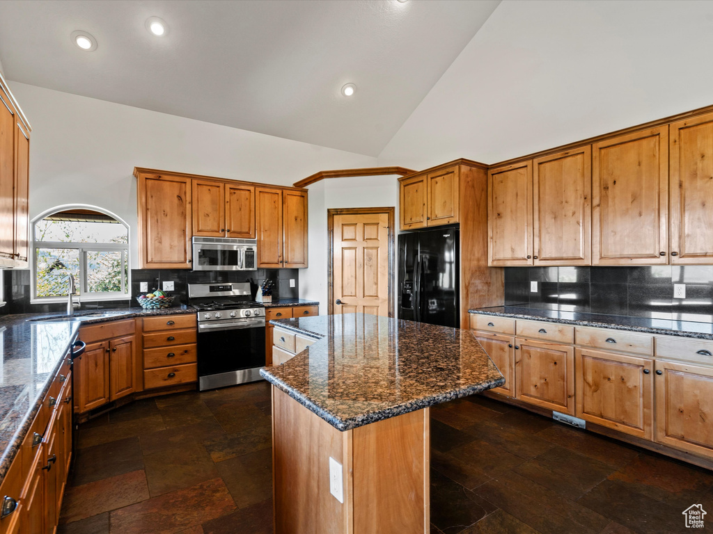 Kitchen with appliances with stainless steel finishes, a kitchen island, decorative backsplash, dark stone countertops, and recessed lighting