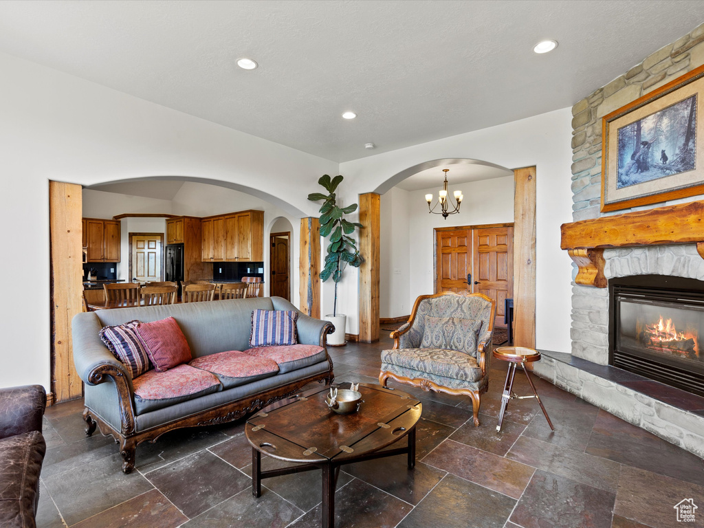 Living room with arched walkways, stone tile floors, a stone fireplace, recessed lighting, and a chandelier